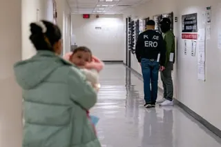a woman carrying a child walks toward two federal agents in the hallway of a courthouse