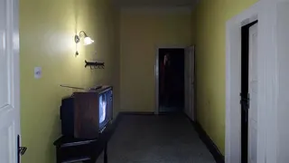 OD image showing yellow room with several doors leading from it. The room has a TV in it, but no chairs
