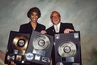 Whitney Houston and Clive Davis hold up a collection of gold and platinum records, celebrating the success of her album I'm Your Baby Tonight