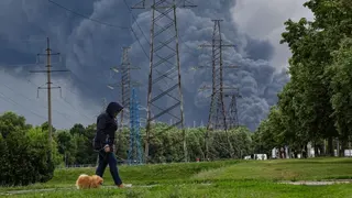 A woman walks in a park as smoke billows in the background following a reported Ukrainian drone attack, in Moscow, Russia, 18 June 2026.