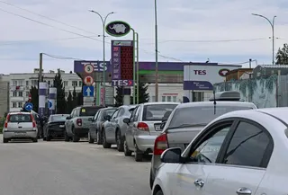 A line of silver and grey cars snaking round from a petrol station where the prices electronic display has no numbers on it.