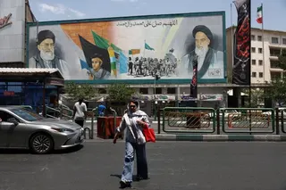 A billboard in a Tehran street displays large portraits of Ayatollah Ruhollah Khomeini and Ayatollah Ali Khamenei as people pass by below.