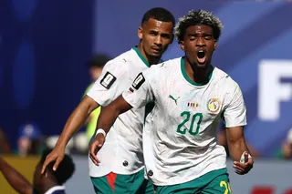 Ibrahim Mbaye celebrates after scoring for Senegal against France in the 2026 World Cup on 16 June. He is wearing a white top and dark green shorts, and his mouth is open as he runs towards the camera.