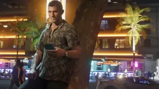 Rockstar Games GTA 6 protagonist Jason Duval lean against a tree in a screenshot from the game, with buildings and cars on the strip behind him lit-up in blue, purple and yellow.