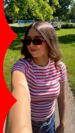 Selfie view of a woman outside wearing sunglasses and stripy top, in a park