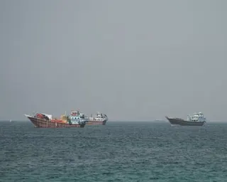 Two large cargo ships anchored in the Strait of Hormuz under an overcast sky
