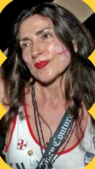 A woman with long dark hair looks at the camera, wearing red lipstick and with the George cross painted on her cheek.