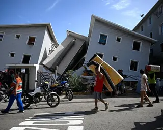 A man carries a mattress past leaning residential buildings in Catia La Mar.