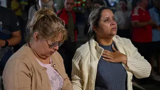 The mother and grandmother of a 18-year-old girl who is feared trapped in a collapsed building in Caracas wait as emergency workers look for her.  The younger woman is holding her hand to her chest while clutching the hand of her mother.