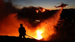 Fire personnel responding to homes destroyed as a helicopter drops water in Pacific Palisades California