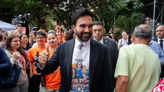 Mamdani shows a thumbs up as he smiles, surrounded by supporters.
