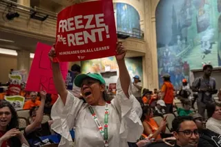 a person cheers while holding a sign that reads 'freeze the rent'