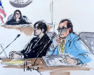 two men sit at table in courtroom as judge watches behind them