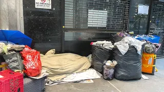 A homeless man sleeping on a New York City street beside his possessions.