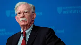Former Trump national security advisor John Bolton appears against a blue background while sitting on a panel.