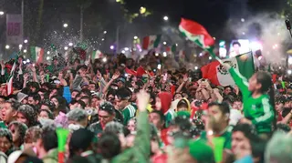 A huge crowd of fans wearing Mexico's green football kit and waving the country's flag celebrate the team's 2-0 World Cup win against Ecuador in Mexico City at night.
