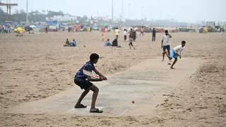 Children play cricket on a beach in India - a batter prepares take a swing at a ball delivered on a rudimentary track.