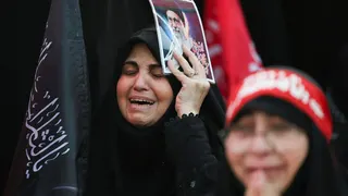 A woman appears to cry as she attends Ayatollah Khamenei's funeral holding a poster of him.