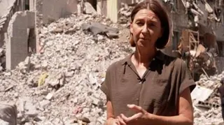 Sarah Rainsford in a brown shirt with short sleeves in front of rubble in Kyiv