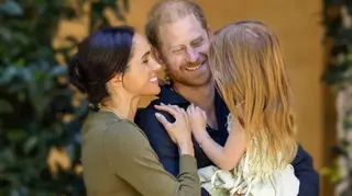 薩塞克斯公爵（Duke of Sussex）與公爵夫人（Duchess of Sussex）身穿休閒服裝相擁，懷抱著穿著夏季連衣裙的莉莉貝特（Lilibet）；她赤著腳、背對鏡頭，留著一頭長長的紅髮。