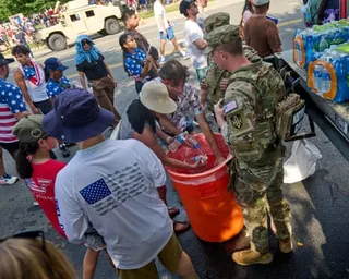people stand outside around bucket with water bottles