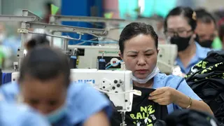 Vietnamese garment factory workers stitch apparel at a factory in Ho Chi Minh City on April 3, 2025. They are seen in a row in light blue shirts bent over white sewing machines.