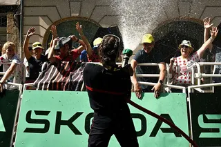 A firefighter sprays water to cool off spectators who wait for riders near the finish line