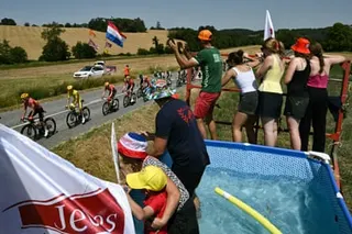 Uno-X Mobility team’s Norwegian rider Torstein Traeen wearing the overall leader’s yellow jersey cycles with the peloton past spectators in a paddling pool