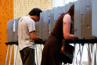 Two people stand at voting booths with privacy dividers in a polling station