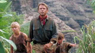 Sam Neill walking through a Jurassic forest, leading two children