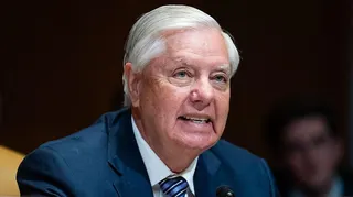Lindsey Graham, wearing a blue suit jacket and white shirt with tie, speaks into a microphone