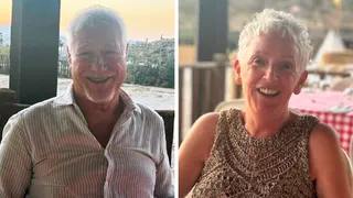 A smiling man and woman sat outside in the sun.