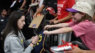 Caitlin Clark of the Indiana Fever signs autographs for fans before a WNBA game against the Phoenix Mercury.