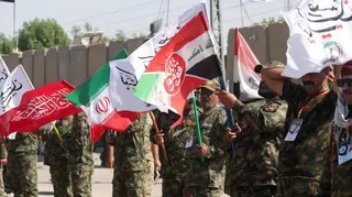 Iranian military personnel stand in a line waving red, white, green and black flags.