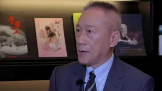 TSMC's Wendell Huang wearing a suit and sitting for an interview, with pictures or books seen on the wall behind him