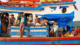 Dozens of Rohingyas including women and children wave solemnly at fishermen from a colourful boat