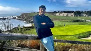 阿尤什·德布站在海邊高爾夫球場前，雙臂交叉拍照。