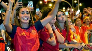 A female celebrates her country's World Cup win with her hands raised in a crowd full of Spanish supporters.