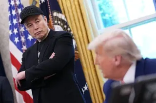 one man stands with his arms crossed as another man sits
