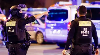 A police officer carrying a machine gun (L) and a colleague talk near the scene where several people were injured on the sideline of the Christopher Street Day (CSD) parade in Berlin, Germany, 25 July 2026.