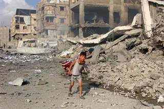 A Palestinian boy carrying a quilt walks past the destroyed buildings at the Al-Jalaa street following an Israeli strike in Gaza City on July 24, 2026