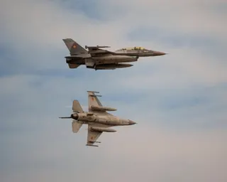 Two F-16 fighter jets fly in formation against a cloudy sky