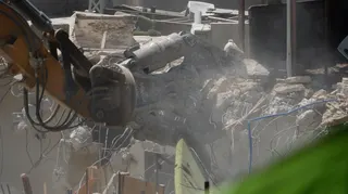 An excavator picks up rubble and wires after the demolition of a building.