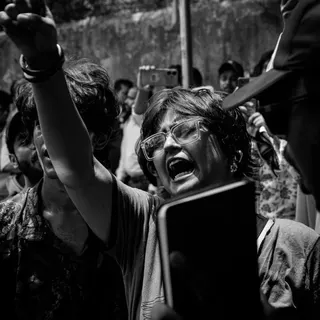 A picture of 22-year-old Sakhi shows her among protesters, arm raised and mouth open as she chants. She has shoulder length hair and glasses.