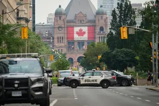 Police vehicles block a street in front of a building with a large Canadian flag displayed on it