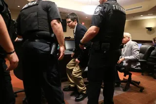 Two sheriff officers escort Colt Gray in sunglasses and business attire in a courtroom setting
