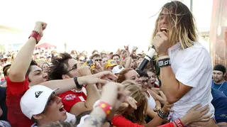 Jared Leto, frontman for Thirty Seconds to Mars, performing in the open air to a crowd of people who are surging forwards. He is singing into a microphone and his hair is sweeping across his face (Photo by J. Shearer/WireImage)