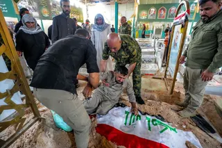 EDITORS NOTE: Graphic content / A mourner reacts by the Iraqi flag-draped grave of Hussein Abbas al-Tamimi, who was killed earlier in Diyala in central Iraq by US-Saudi strikes on Hashed al-Shaabi forces, after his burial at the Badr organisation's district in the Wadi al-Salam cemetery in the central holy city of Najaf on July 29, 2026.