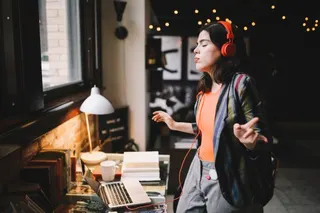 Young Latinx woman sitting at the desk in her Los Angeles apartment, receiving happy news over the social networks or just having a nice day, dancing to the music.