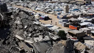 Palestinians walk past the rubble of residential buildings destroyed during the Israeli offensive as displaced people shelter in tents, in Gaza City, July 4, 2026.